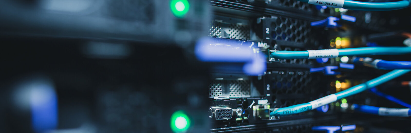 Ein Netzwerkserver mit sichtbaren Kabeln und Lichtern. Die Kabel sind in verschiedene Ports eingesteckt, und einige grüne Lichter leuchten. Der Fokus liegt auf der Verbindungstechnologie des Servers, die für die Datenübertragung und -verarbeitung entscheidend ist.