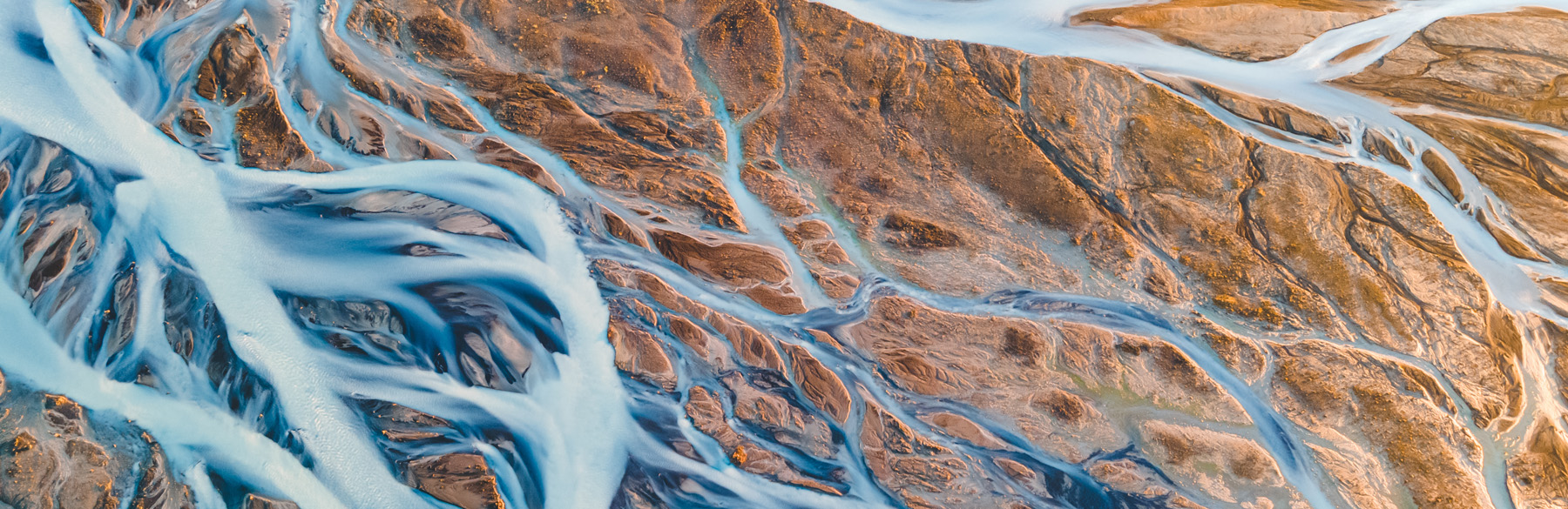 Eine luftige Ansicht einer Landschaft mit braunen Erden und blauen Wasserläufen, die sich wie Adern durch die Fläche schlängeln. Die verschiedenen Formen und Farben schaffen ein interessantes, texturiertes Muster, das die natürliche Bewegung des Wassers und die Erdoberfläche zeigt.